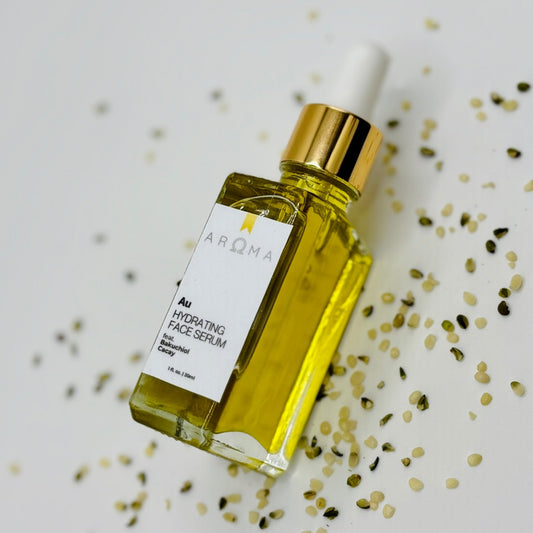 A clear glass bottle with a white dropper filled with yellow liquid, labeled 'AROMA', placed on a surface with scattered seeds around it.